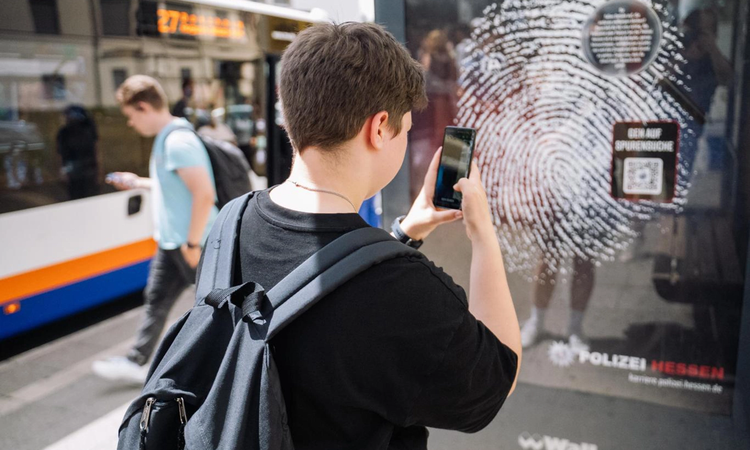 Person an einer Buswartehalle interagiert mit Recruiting-Kampagne durch das Scannen eines QR-Codes auf einem City Light Poster.