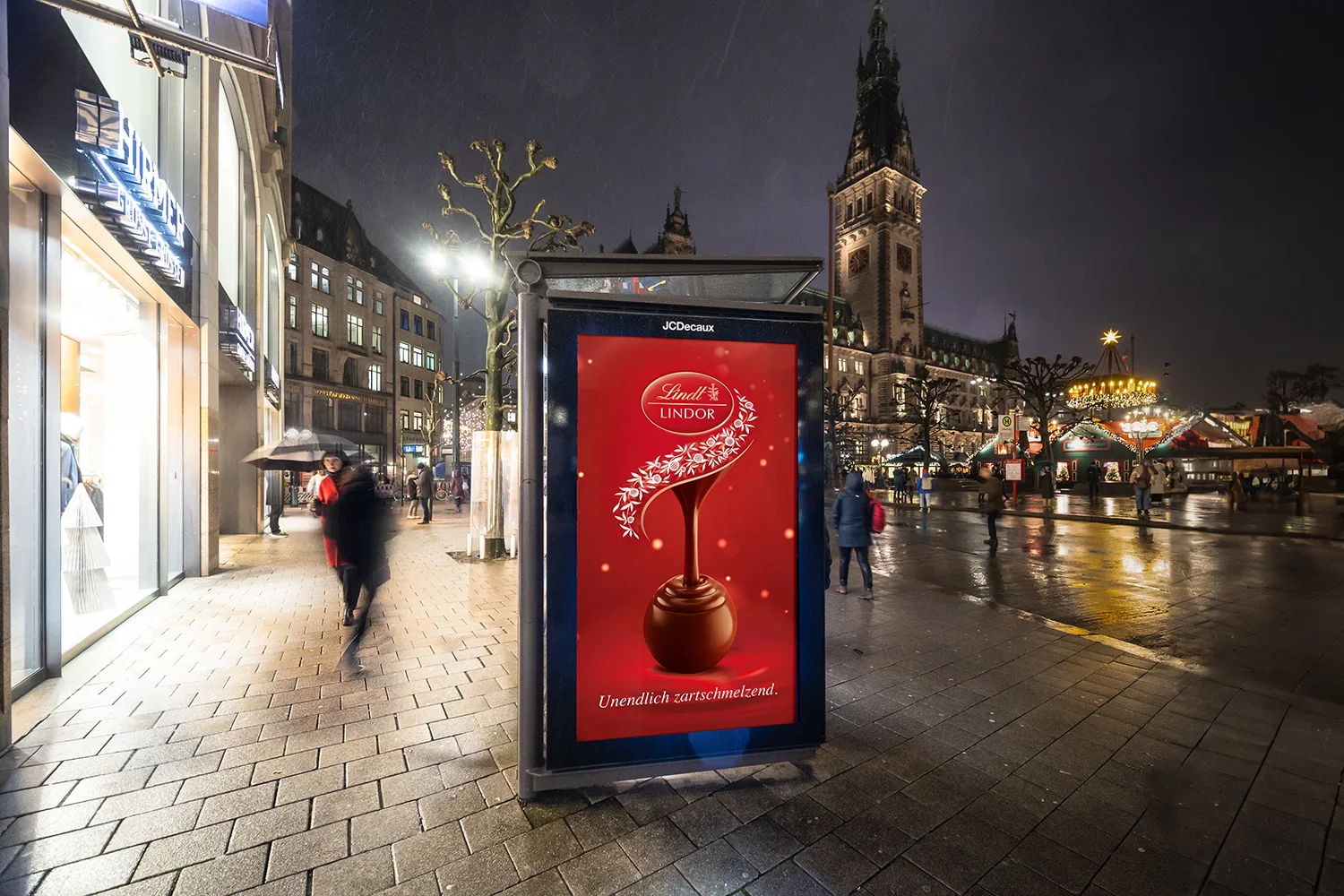 City Light Poster Schokoladenwerbung am Rathausplatz im Hamburg am Abend zur Winterzeit mit Weihnachtsmarkt im Hintergrund