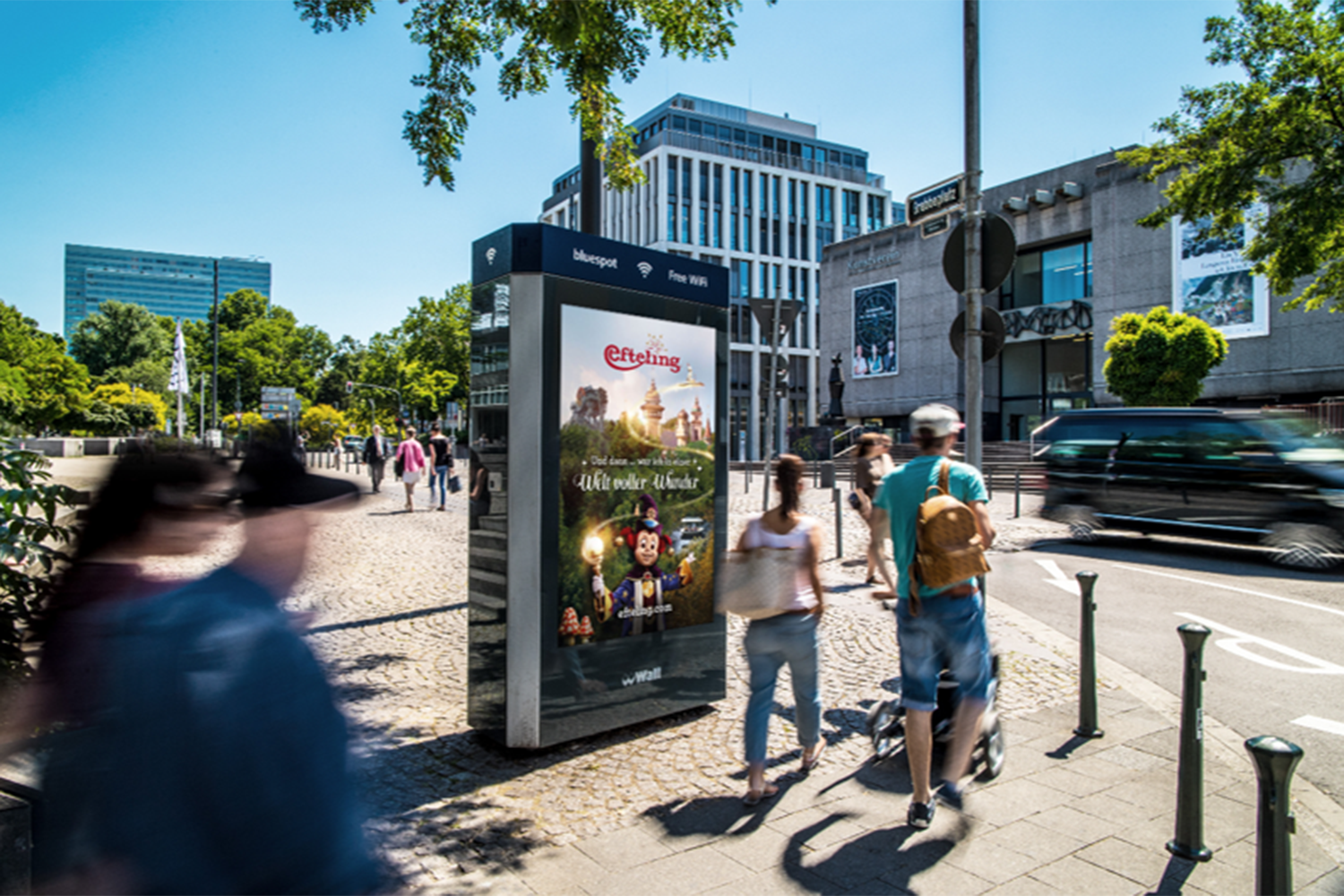 Digital City Light Poster mit Freizeitpark Werbung im sommerlichen Stadtalltag.