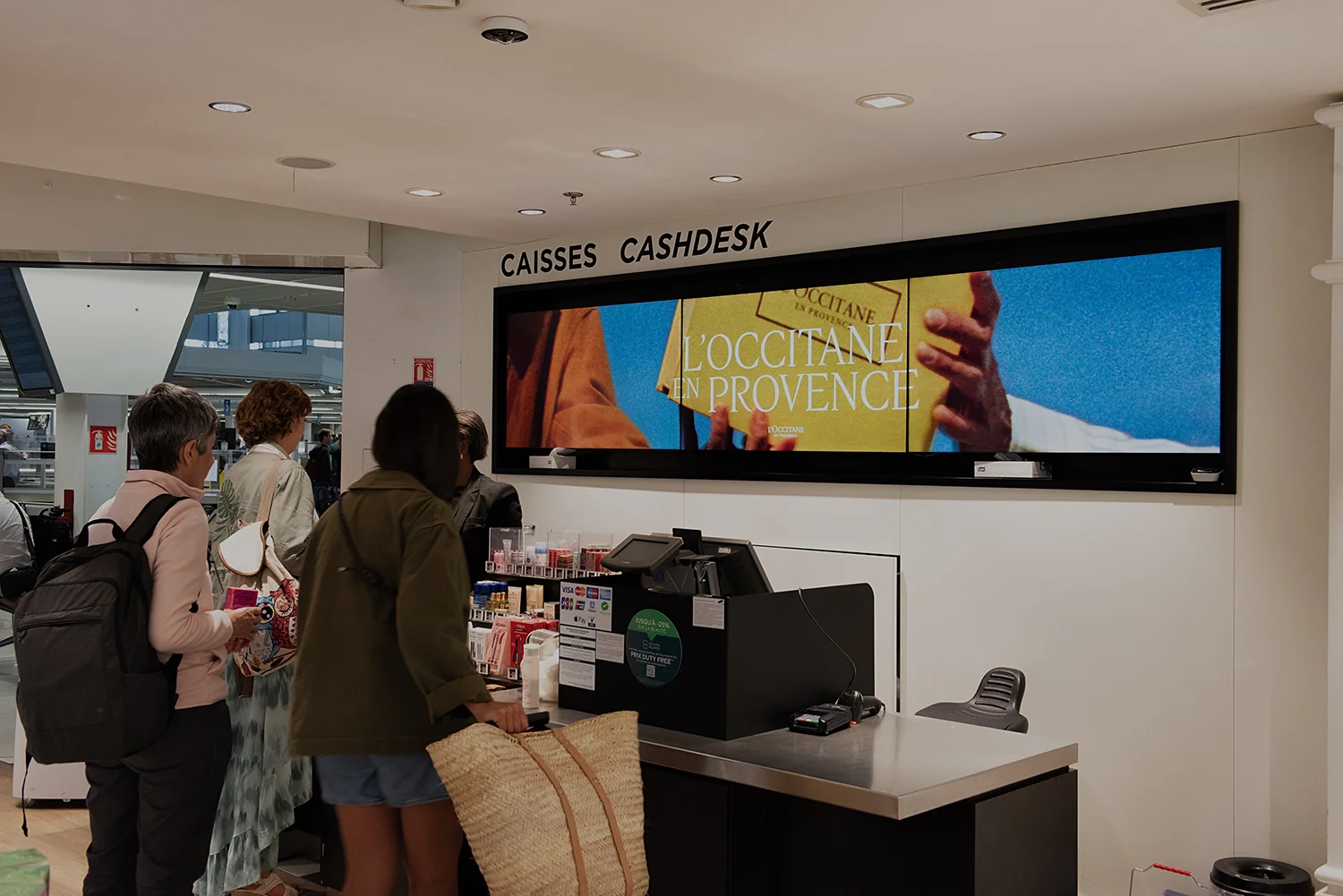 Digitaler Werbeträger hinter einem Counter am Flughafen in Paris zeigt Kosmetikwerbung.