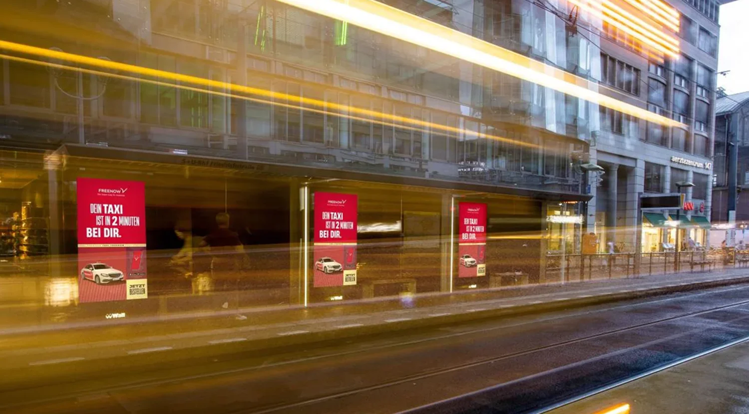 Drei Digital City Light Poster zeigen Fahrdienst-Werbung in Berliner Friedrichstraße bei Dämmerung.