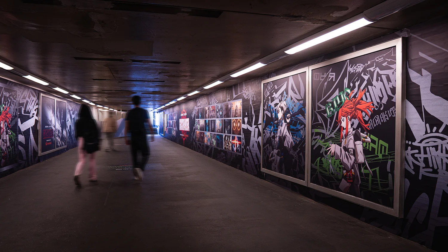 Drei Menschen laufen im Fußgängertunnel mit Grafitti und Animemotiven an den Wänden.
