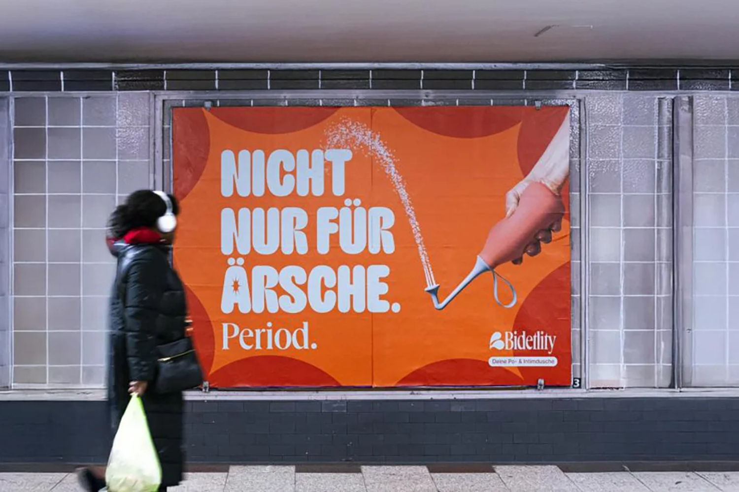Großes Plakat hinter U-Bahn-Gleis mit Werbung für Hygieneartikel in Berlin. Eine Frau steht im Vordergrund und betrachtet das Plakat.