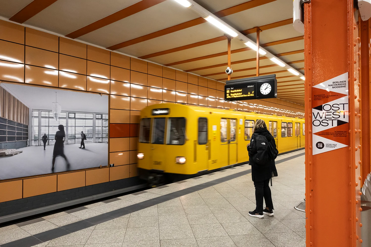 Person wartet in U-Bahnhof während Zug einfährt, Hintergleisflächen zeigen Kunstprojekt des Landesdenkmalamts Berlin und der Berliner Verkehrsbetriebe.