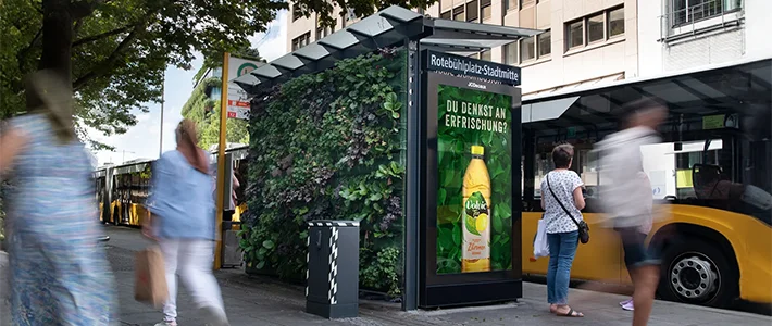 Digital City Light Poster in Bus-Wartehalle mit Grünwand zeigt Getränkewerbung am Rote Bühl Platz in Stuttgart.