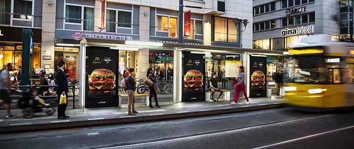 Drei Digital City Light Poster an Tram-Wartehalle in der Berliner Friedrichstraße zeigen Werbung einer Fast Food-Kette.