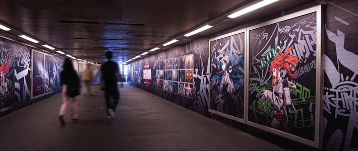 Drei Menschen laufen im Fußgängertunnel mit Grafitti und Animemotiven an den Wänden
