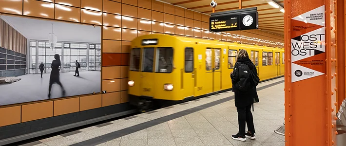 Person wartet in U-Bahnhof während Zug einfährt, Hintergleisflächen zeigen Kunstprojekt des Landesdenkmalamts Berlin und der Berliner Verkehrsbetriebe.
